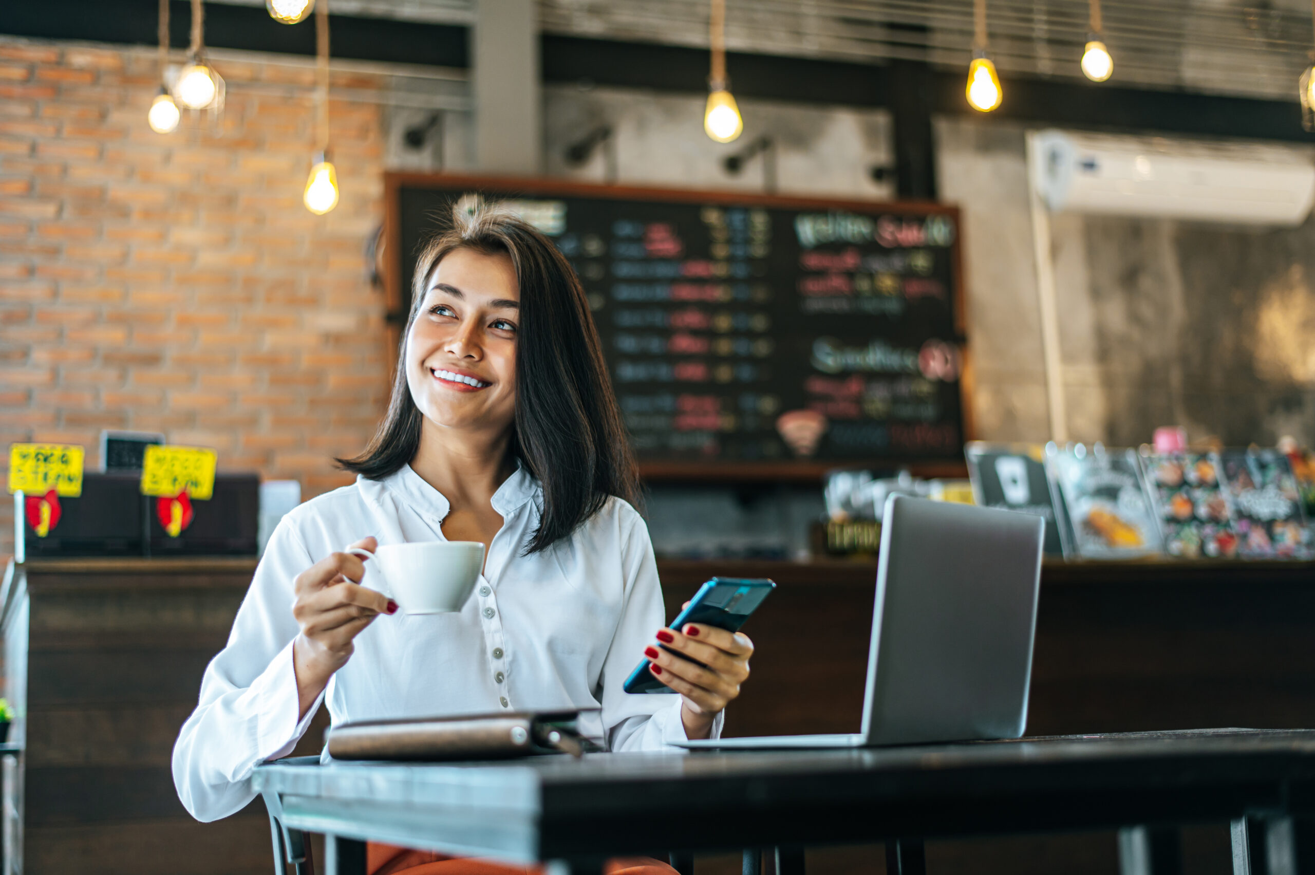 woman-sitting-happily-working-with-smartphone-coffee-shop-notebook-Faturamento-de-franquias-cresce-21-em-Curitiba-Londrina-tambem-regista-aumento-scaled.jpg